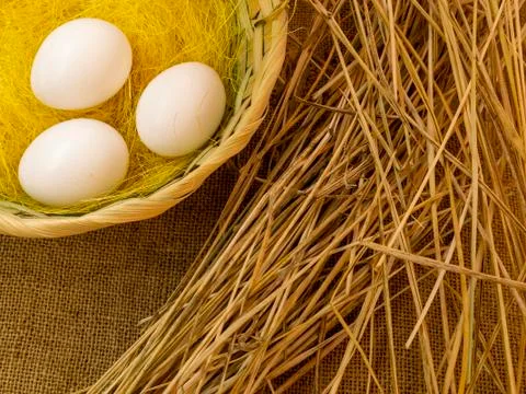 Three eggs in a basket on burlap next to the straw. Stock Photos
