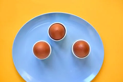 Three Eggs in Egg Cups on Blue Plate Yellow Background Stock Photos