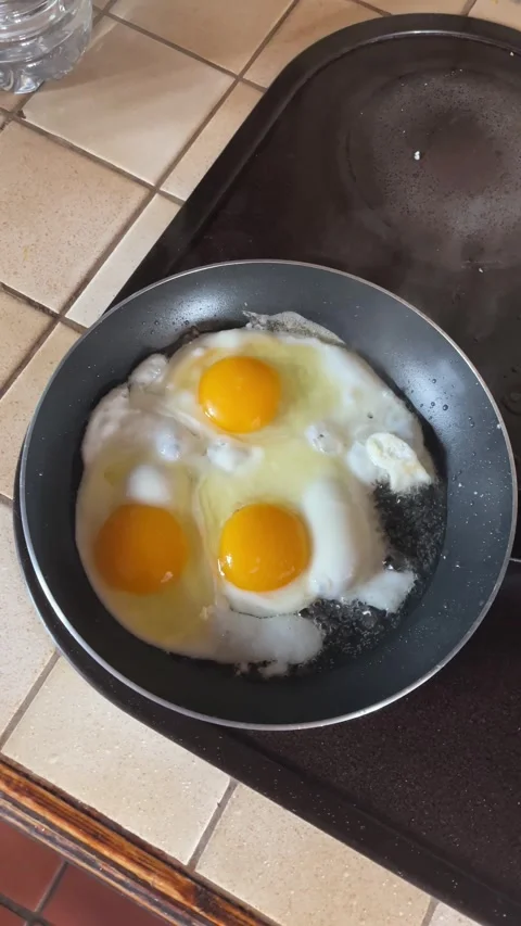 Three eggs frying in hot oil, with fat exploding and hot oil splashing around Stock Footage 334048158