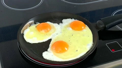 Three eggs with ground pepper frying on pan Stock Footage 130207032