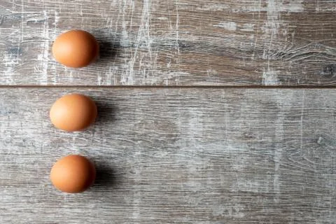 Three eggs in a vertical row with shadows on wooden background Stock Photos