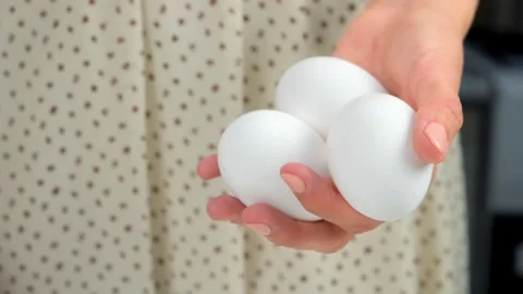 Three eggs in woman hands on kitchen at home ready to cook food. Video stock 313124319