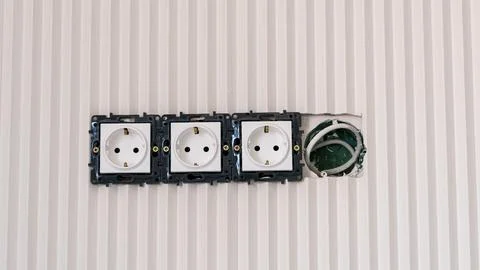 Three electrical power outlets mounted on a wall with one outlet partially .. Stock Photos