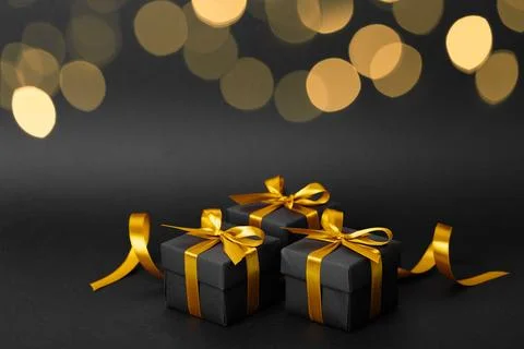 Three elegant black gift boxes with gold ribbons on a black background Foto stock