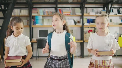 Three elementary school girls, each carrying a backpack and books, walk together Stock Footage 284275254