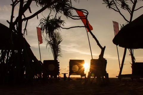 Three empty deck chair silhouettes at sunset beach, red flags waving Stock Photos