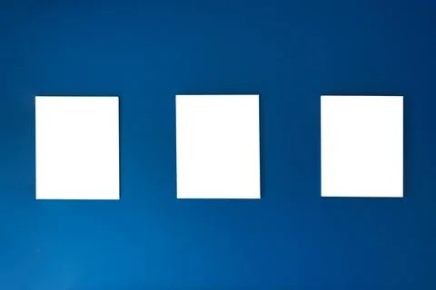 Three empty square canvas frames arranged on deep blue wall Foto stock
