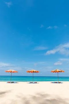 Three empty sunbeds and beach parasol sunshades on sand beach Stock Photos
