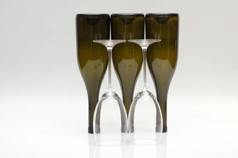 Three empty upturned wine bottles and two glasses on a white background. Stock Photos