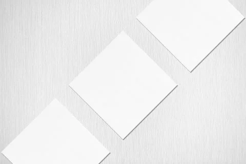 Three empty white square business card mockups lying diagonally on grey backg Stock Photos