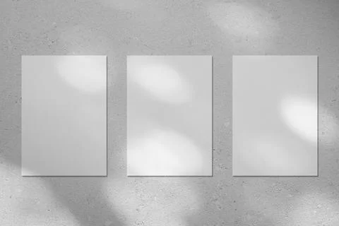 Three empty white vertical poster mockup with diagonal window shadow on the wall Stock Photos