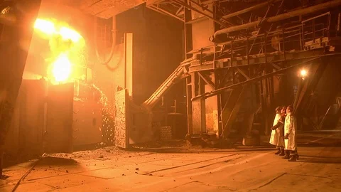 Three engineers in overalls are discussed in front of a flaming liquid metal  Stock Footage 105840076