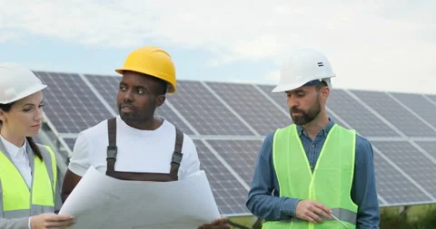 Three engineers in special suits walk among rows of solar panels and inspect Stock Footage 139231658