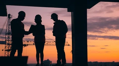 Three engineers work on a construction site on a sunset background. Construction Stock Footage 117633040