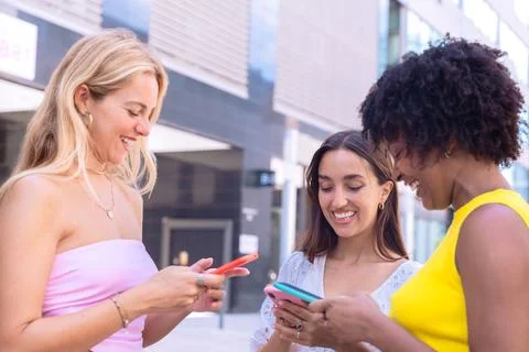 Three excited friends looking at a smartphone outdoors. Stock Photos