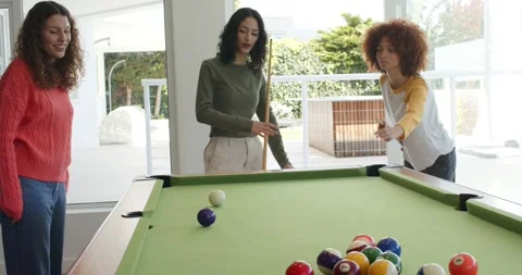 Three female friends lining shot, striking ball, cheering around pool table in Stock Footage 344339988