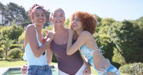 Three female friends posing, hugging and laughing at backyard pool in swimwear Stock Footage 342234081