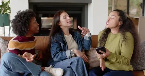 Three female friends sitting on couch in living room watching smartphone cue, Stock Footage 340655079