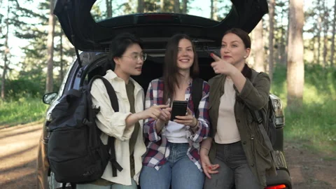 Three female friends using a smart phone for navigation on a forest road trip 스톡 동영상 335843513