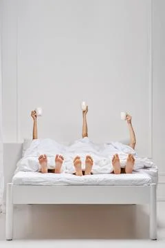 Three female hands in bed holding cup of fresh coffee over the blanket Foto stock