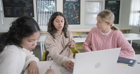 Three female students in class, center typing on white laptop explaining for Stock Footage 340898520