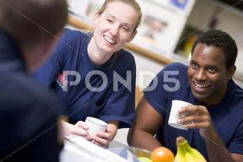 Three firefighters in break room drinking coffee and talking (selective focus) Stock Photos
