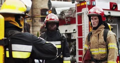 Three firefighters of different races in helmets and protective suits discussing Stock Footage 137896721