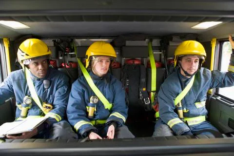 Three firefighters in fire engine wearing helmets with one reading Stock Photos