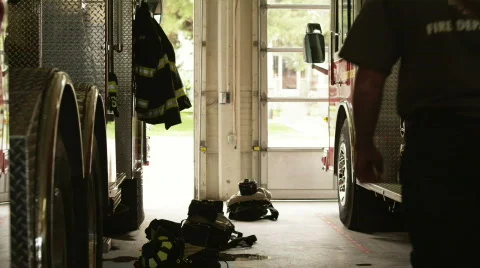 Three firefighters putting protective suits standing by fire engine in garage Stock Footage 866704