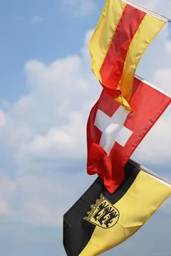 Three flags on the flagpoles - waving in the wind. Flags of Baden, Switzerl.. Stock Photos