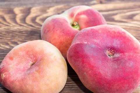 Three flat saturn peaches close up view arranged on a dark structured wooden  Stock Photos