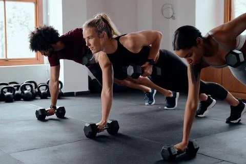 Three focused young adults in a row doing plank exercises with weights at the Stock Photos