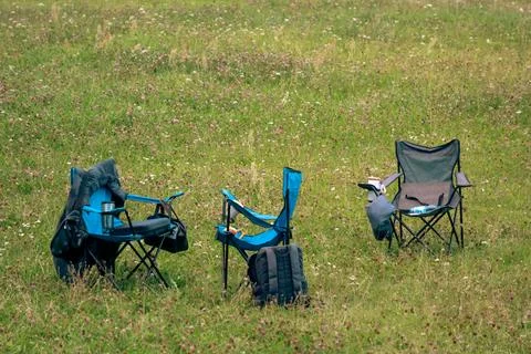 Three Folding Camping Chairs Set Up on Grassy Meadow Field Stock Photos