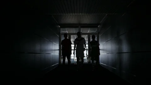 Three football players are walking along a dark tunnel to the football field. Stock Footage