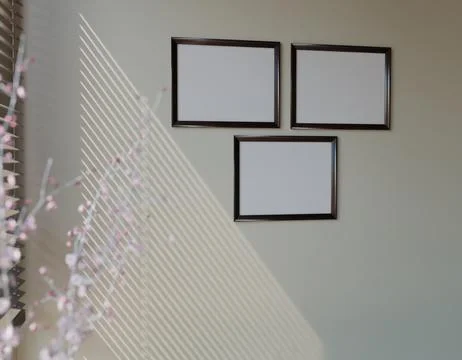 Three framed, blank canvases on a light beige wall, illuminated by sunlight.. Stock Illustration