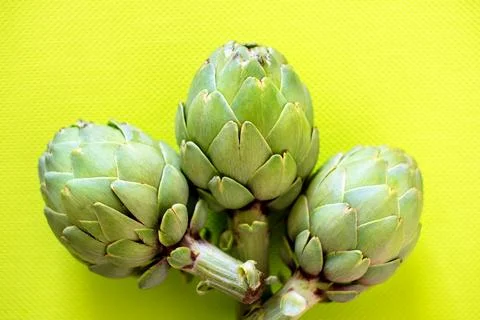 Three fresh artichokes resting on a vibrant yellow surface, showcasing their  Foto stock