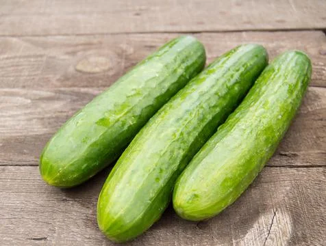 Three fresh cucumber lying on an old wooden background Stock Photos