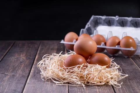 Three fresh egg on the straw, with a full package of eggs in the background.  Stock Photos
