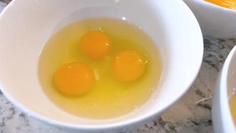 Three Fresh Eggs Cracked Open in a White Bowl for Cooking Foto stock