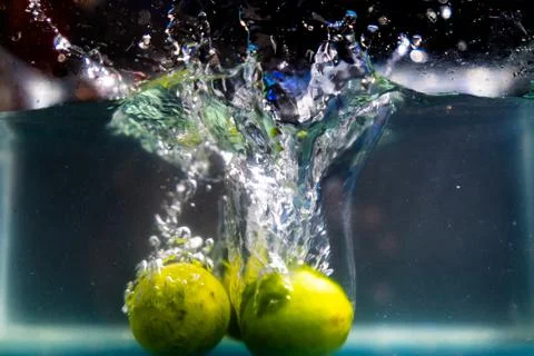 Three fresh limes falling deep in water with splash Stock Photos