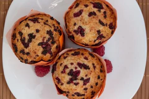 Three fresh muffins with raspberry are lying on a white plate. Close up. Stock Photos