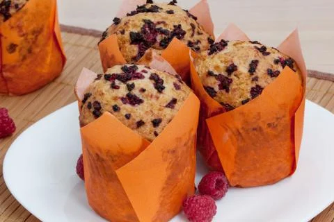 Three fresh muffins with raspberry are lying on a white plate. Close up. Stock Photos