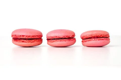 Three fresh pink macarons with dark berry filling arranged in a row on a wh.. Stock Photos