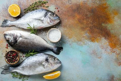 Three fresh raw Dorado fish with spices and olive oil on a blue rusty table.. Stock Photos