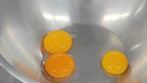 Three fresh raw egg yolks in a stainless steel mixing bowl. 스톡 동영상 339200516