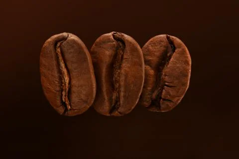 Three fresh roasted coffee beans isolated on a brown background. macro. Stock Photos