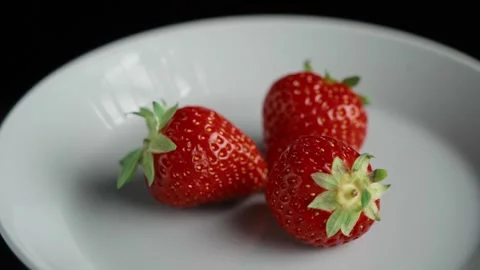 Three fresh strawberries on plate rotating close up Stock Footage 345733458