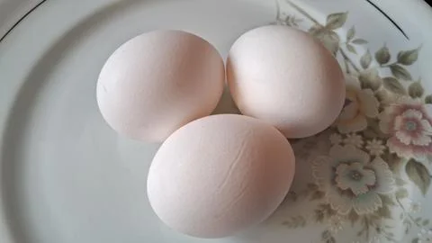 Three fresh white eggs on a plate. Raw chicken eggs ready for cooking in a Stock Photos