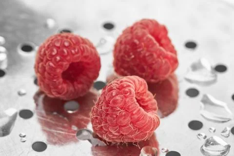 Three freshly washed raspberry berries lie on a metal surface Stock Photos