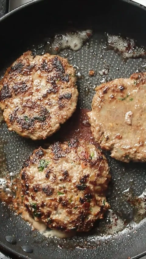 Three fried beef burger patties in a frying pan Stock Footage 303934678